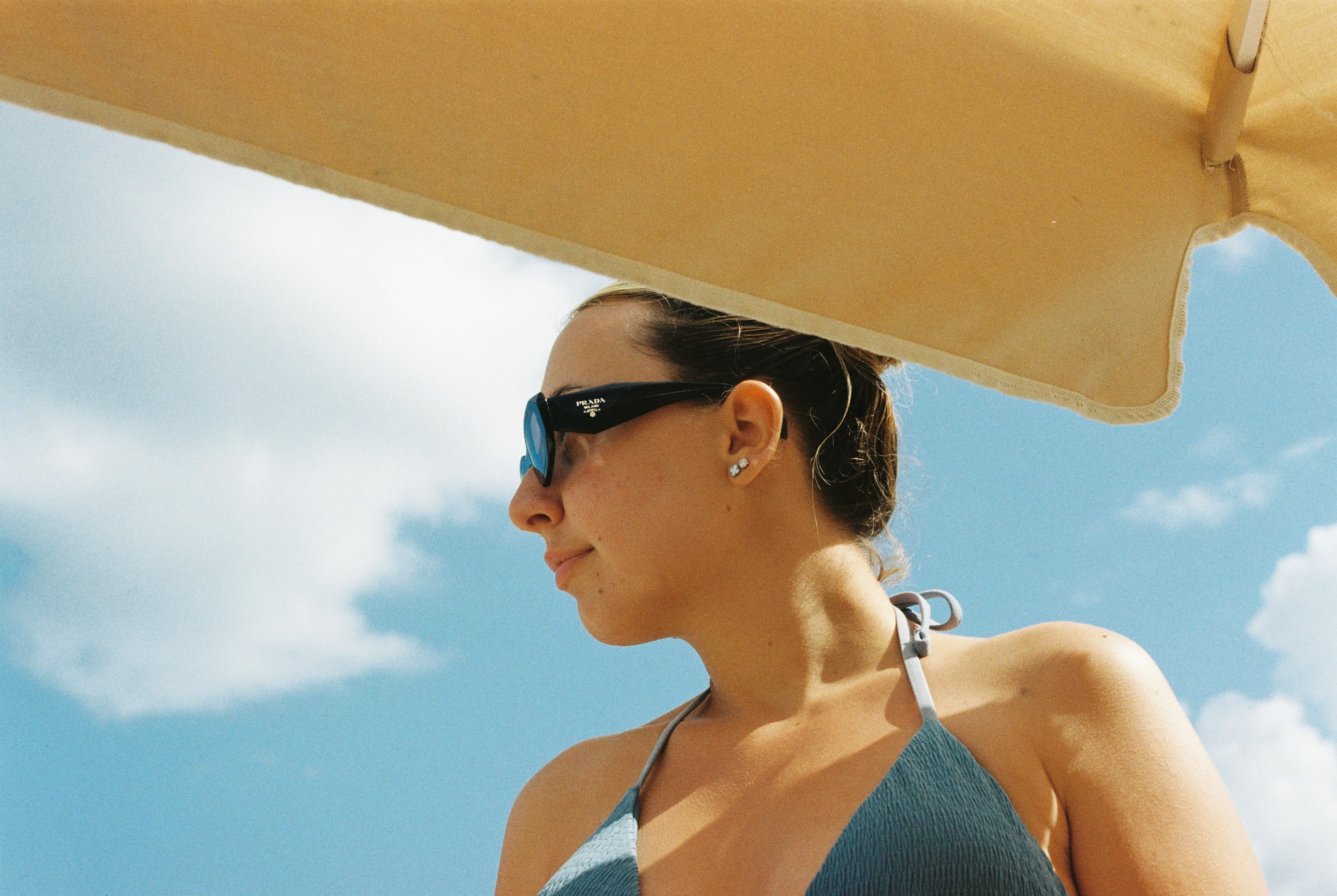 Figure resting under a beach umbrella against a blue sky
